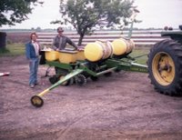 Man and Woman Stand Behind Trailer with Chemicals Pulled by Tractor