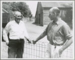 Two men talking by a low wire fence