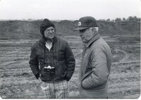 Two men stand near earthmover in a field