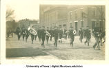 Marching band walking past brewery, Homecoming parade, The University of Iowa, 1917