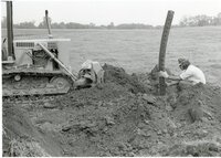 1979  Man on Bulldozer in front of Man putting pipe in the ground