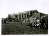Fence backstop with spectators in Clyde Williams Field behind the State Gymnasium.