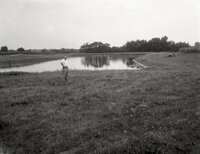 Man stands by farm pond holding hat