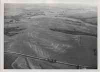 Wide aerial view of contoured farmland showing a road, stream, and trees