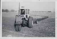 Man on tractor in enclosed cab cultivates field.