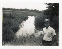 1986 Bill Walker stands by water  in field