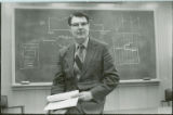 George Burnet seated before blackboard, 1973