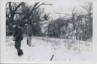 Two unidentified men stand in the snow looking toward an enbankment while another man walks in the opposite direction