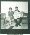 Man reading newspaper and making a face sitting next to a woman, 1960s