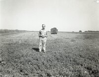 Unidentified man wearing glasses with hands behind his back stands in field