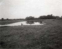 Man stands by farm pond holding hat