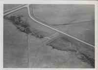 Aerial View of farmland with road running through it and trees off to the left.