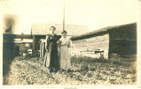 Mother and daughter by farm buildings, Iowa?, 1910s