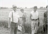 Four unidentified men stand in field by highway