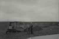 Two men standing in field by bulldozer
