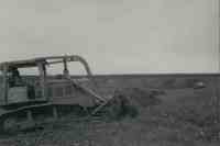 Two men standing in field by bulldozer