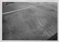 Aerial view of contoured, sloped farmland with farm buildings in the left hand corner and roads on the right