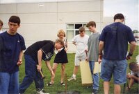 1999 Students watch Ben Schwenk drive a stake into the ground in preparation for planting a tree while students watch