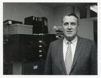 1970s Unidentified man in suit stands in office