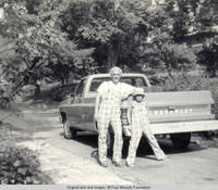 Bill and John, Jr. wearing a hat, leaning on truck