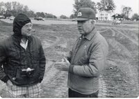 Two men stand near earthmover in a field
