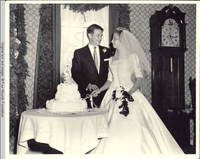 Frindy and John, Sr. cutting the wedding cake, facing each other, in dining room 