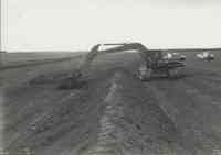 Man beside truck watching Komatsu Excavator at work in field