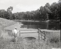 Man stands by drainage pipe by pond