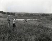 Two unidentified men stand in field by pond