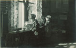 Small children stand near a window looking at a plant and a fishbowl, The University of Iowa, 1920s