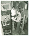 Physics students between tank and controls of 2 MeV Van de Graaff accelerator, The University of Iowa, 1963