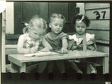 Girls writing and playing at a table outside, The University of Iowa, May 10, 1941