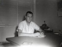 Unidentified man sits at desk holding pen