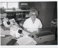Woman in Glasses Sits at a Desk Behind Typewriter
