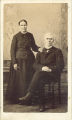 Woman posed standing next to seated man with white hair and beard, Lansing, Iowa, 1900s