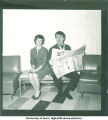 Man reading newspaper and making a face sitting next to a woman, 1960s