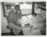 Unidentified Smiling Man with Glasses Sits at Desk in Office