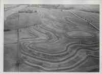 Aerial view of contoured, sloped farmland with farm buildings in the left hand corner and roads on the right