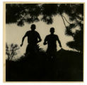 Two runners silhouetted against trees and a building