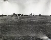 Grassy field with farmhouse and  buildings in background