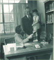 Man holds a young girl standing on a desk in an office, The University of Iowa, 1940s