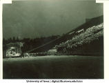 Man speaking on a stage in a stadium at night, The University of Iowa, 1940s