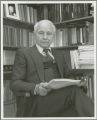 Earl O. Heady, seated in front of shelves of books, 1982