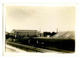 Runners stretching on the southwest side of Clyde Williams Field, with the State Gymnasium in the background