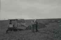 Two men standing in field by bulldozer