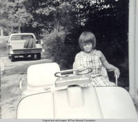 John, Jr. in golf cart with hand on driving bar, looking down
