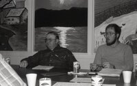 Two unidentified men sit at a table listening at a meeting