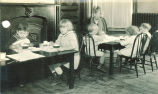 Children sitting at small dinner tables with a woman, The University of Iowa, 1920s