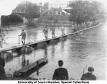 Military personnel walking across bridge over Iowa River constructed by cadets, The University of Iowa, 1929