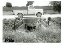 Wilbur Allender standing in front of road culvert structure, 1956